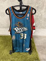 Front view of Champion Detroit Pistons basketball jersey, showing flaming horse logo, Pistons text, and number 33 with visible discoloration/stains.