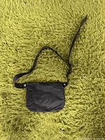 Black small waist pouch on green carpet front side showing snap button flap and adjustable strap