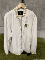 Front view of white Versace windbreaker jacket showing zipper, embroidery on left chest, and Greek key trim on collar, cuffs, and hem.