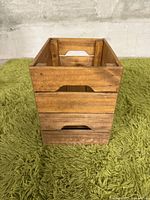 Front view of one wooden storage crate showing slatted design and cutout handle.