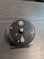 Top side of the fly fishing reel showing the 'Marvel' brass badge and a brass key with 'Made in England' marking, revealing vintage alloy body with some wear.