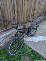 Black BMX bike leaning against a wooden fence showing overall bike condition and frame shape.