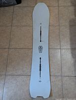 Bottom side of the Burton Skeleton Key snowboard showing white surface with graphic elements and model detailing.