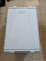 Top view of white lid showing Coleman logo and textured surface on a rectangular electric cooler.