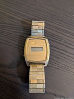 Front view of Unik Time digital watch showing rectangular gold-tone case and metal expandable band.