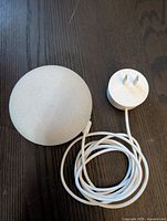 Top view of Google Nest Mini smart speaker and white power adapter placed next to it on a dark surface.