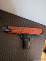 Photo shows Hilti DX 36 powder actuated tool lying on a wooden surface; visible wear and dirt on tool casing; orange and black color scheme; pistol grip design and model markings clear.