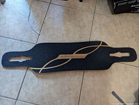 Top side of the longboard showing black grip tape with Limitless logo and decorative wave design.