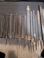 Top view of assortment of metal files arranged in a row on dark surface showing different file shapes and sizes.