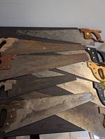 Several vintage hand saws arranged overlapping on a flat surface, showing metal blades and wooden and plastic handles with rust and wear.