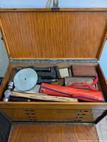 Open wooden tool chest showing lid compartment with hammers, planes, red-handled hammer, small wood blocks