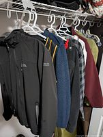 Overview of men's clothing items hanging on hangers in a closet rack, showing jackets, sweaters, and shirts, providing condition and variety detail.