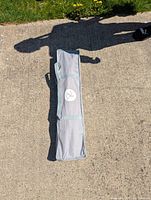 Folded travel bed inside grey carrying case with handles, placed on concrete outdoors.