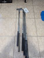 Two putters, three wedges, and one iron golf club laid out on tile floor showing grips, shafts, and club heads.