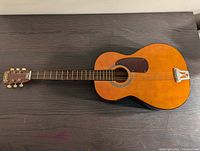 Full view of vintage wooden folk guitar with natural finish and brown pickguard.