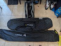 Three bags arranged on floor: Wedze black ski bag, Burton black multicolored dot snowboard bag, Head black and gray ski boot bag