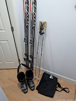 Full ski lot including Fischer skis, ski poles, ski boots, and ski bag laid out against wall and floor.