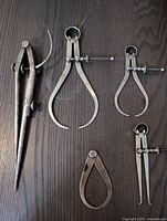 Five metal calipers of different sizes shown on a dark wood surface