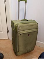 Front view of light green SwissGear suitcase showing telescoping handle extended, front zippered compartments, and logo patch.