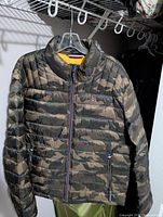 Front view of Tommy Hilfiger camouflage packable jacket hanging on a hanger, showing the full zipper closure and zipped pockets.