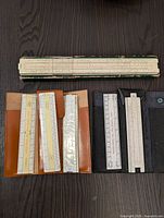 Top-down photo showing all sliding rules arranged on dark surface with cases, highlighting sizes and condition.