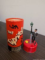 Photo of The Tipitoi vintage wind-up toy beside its original red cylindrical packaging container.