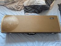 Closed tan hard case with black handle and latches, showing scuffs and wear marks.