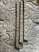 Three antique hand forged golf clubs with original wood shafts laid out on a fabric surface.