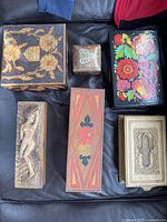 Seven decorative boxes arranged on a black surface showing different carvings and paint styles