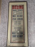 Framed boxing poster showing event details and fighter names with visible glass breakage.