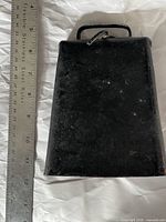 View of first antique cow bell next to ruler for scale, showing trapezoidal shape and handle