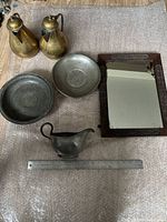 Overview photo of six items including pewter dishes, gravy boat, two bronze jugs, framed mirror, and pewter chargers.