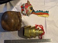 Photo showing three items: a carved wooden percussion instrument, a colorful dragon head decoration, and brass wind chimes.