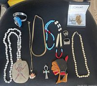 Full lot shown on black textured surface, displaying all jewelry pieces including necklaces, rings, cufflinks in box, and bracelets.