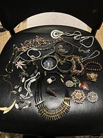 Overview of assorted jewelry pieces laid out on a black surface, showcasing various necklaces, bracelets, earrings, rings, and pendants in multiple styles and colors.