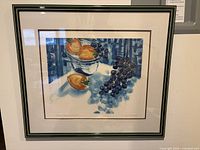 Framed signed print showing a still life of persimmons, grapes, and a bowl in blue tones.
