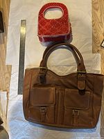 Both handbags shown together with metal ruler for scale: large brown leather handbag and smaller red/white beaded handbag