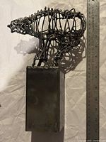 Front view of metal wire sculpture resembling a bear next to an 8-inch ruler for scale, on metal rectangular base.