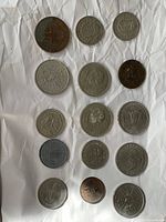 Top view of 15 coins laid out on a wrinkled white paper background, showing various designs and details including a visible 1806 date on Britannia coin.
