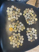 Photo showing multiple groups of international coins spread out on a black leather surface.
