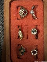 Tray holding six gold-tone rings with various simulated gemstones and clear rhinestones