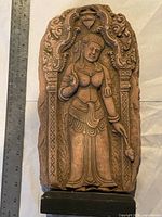 Front-facing view of sandstone carving showing full figure of Buddhist goddess with a ruler for scale measuring approximately 12 inches tall. Mounted on black wooden stand.
