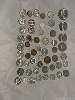 Top view of a flat layout of 52 assorted North American coins, predominantly silver and some copper tones, including different sizes and historic designs.