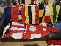 14 vintage Canadian Navy maritime signal flags in various colors and patterns laid out on black leather seating.