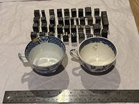 Two vintage blue and white Chinese teacups placed next to 39 metal printing press stamps with Chinese characters, ruler for scale