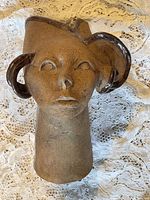 Front view of the vintage clay bust sculpture showing face, eyes, mouth, nose, and looped handles with glazed dark accents.