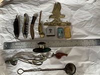 Overview photo showing entire lot on white background with ruler for scale including knives, figurine, candle holder, pipe, whistle, matchbox holders.