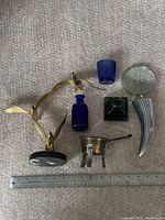 Top view showing all six pieces including the brass bird sculpture, three glass containers, magnifying glass, and small pot with ruler scale for size reference.