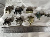 Overview of all 7 vintage metal figurines including 3 dogs, 1 turtle shell, 1 turtle, bird on branch, and cluster of birds shown alongside a ruler for size reference.