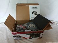 Original box containing electric winch, mounting plate, wiring and owner's manual visible inside.